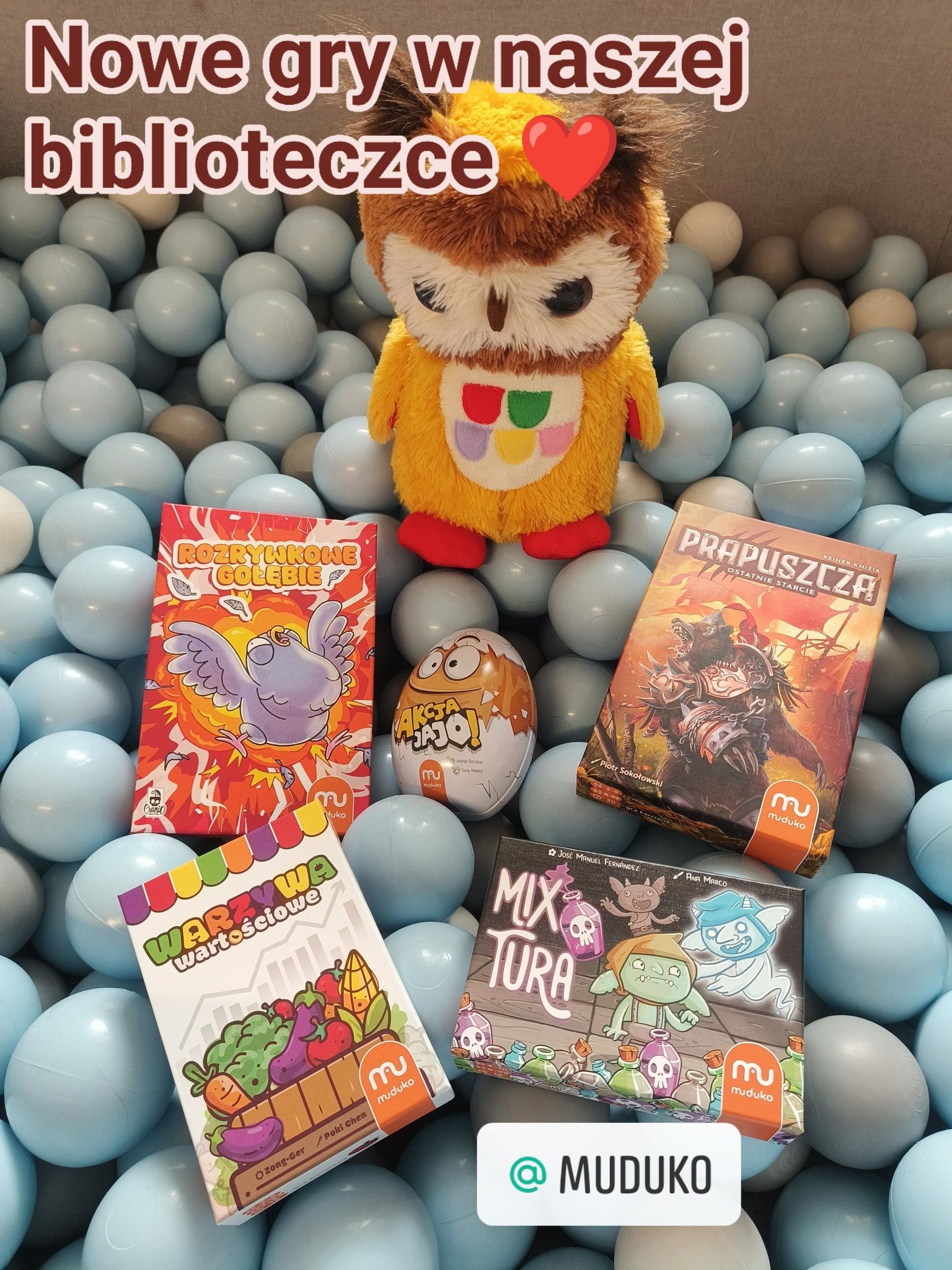 Pięć nowych gier planszowych. Ułożone na plastikowych kulkach w kolorze niebieskim. Za grami stoi kolorowa maskotka sowy.