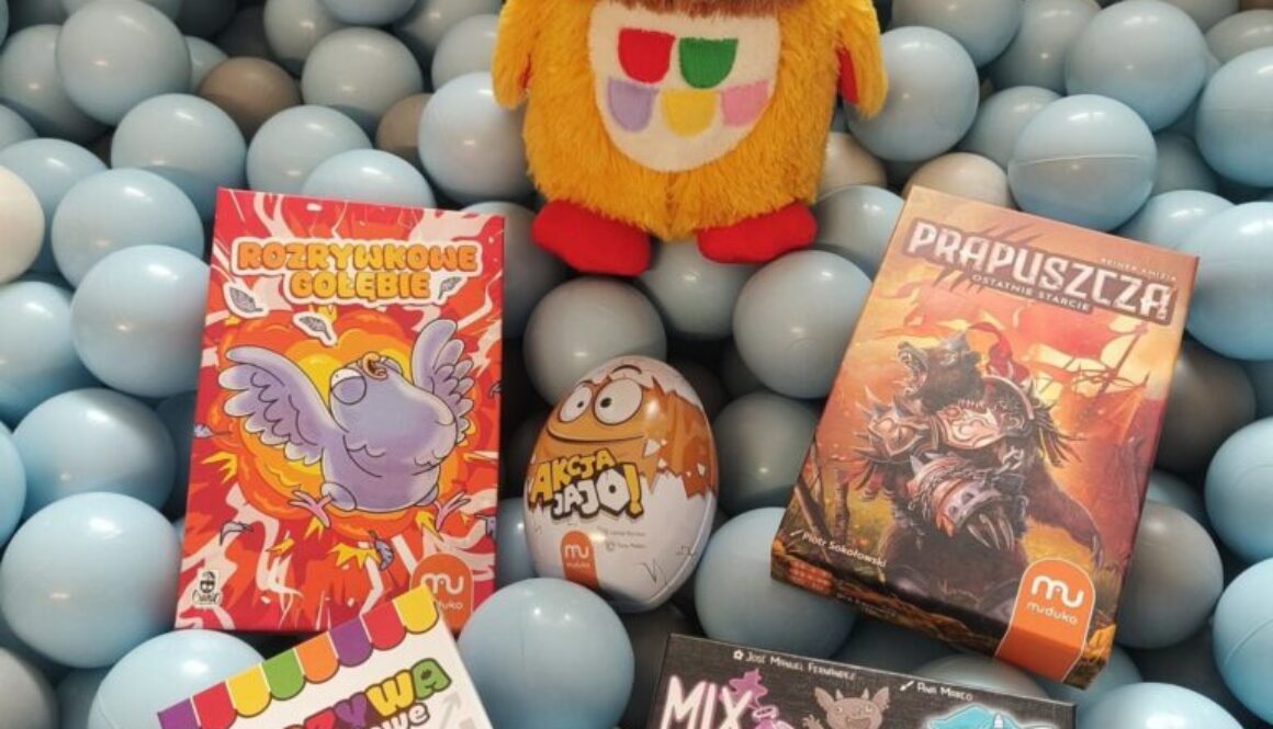 Pięć nowych gier planszowych. Ułożone na plastikowych kulkach w kolorze niebieskim. Za grami stoi kolorowa maskotka sowy.